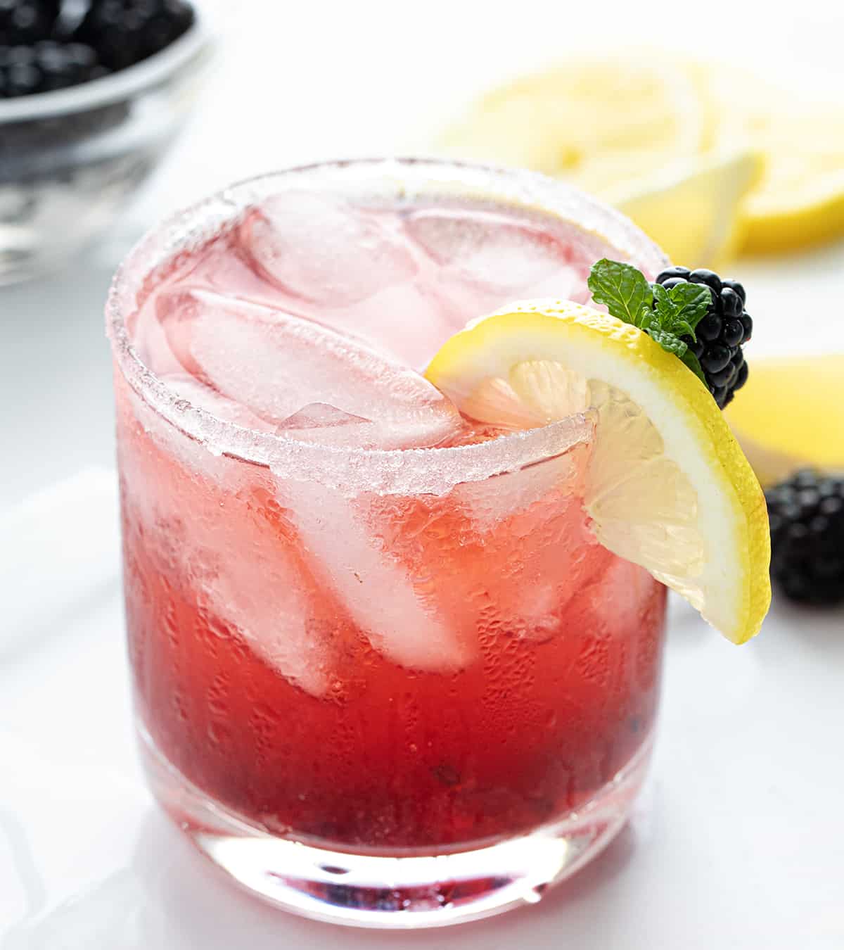 One Blackberry Moscato Cocktail on a Counter with Lemons and Blackberries.