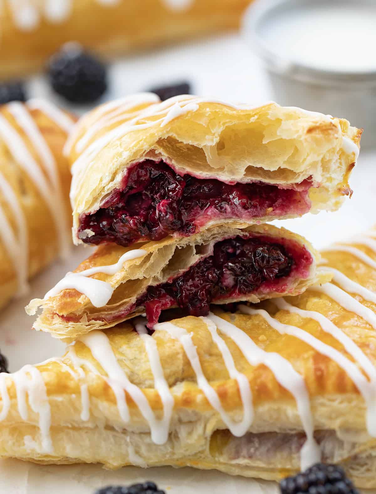 A Cut in Half Blackberry Cream Cheese Turnover on Top of a Whole Blackberry Cream Cheese Turnover on a White Counter.