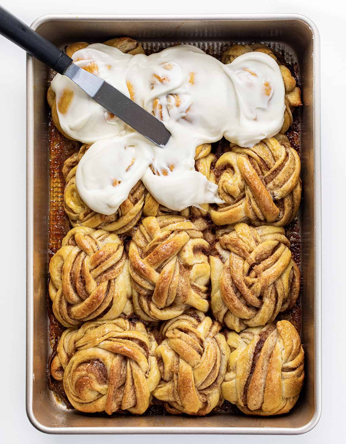 Braided Cinnamon Rolls in Pan After Baking Showing Them Partially Frosted. 
