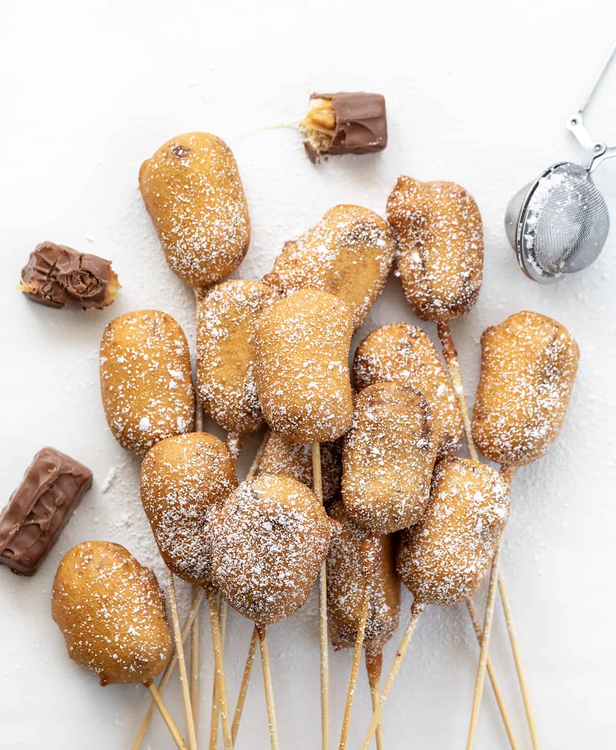 Several Deep Fried Snickers Still on the Skewer on a White Counter.
