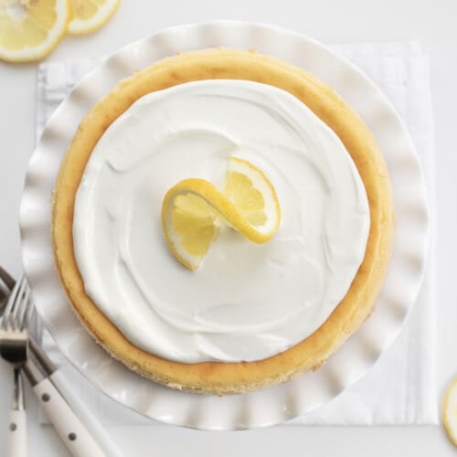 Overhead Image of a Lemon Cheesecake on a White Cake Stand with a Ruffled Edge.