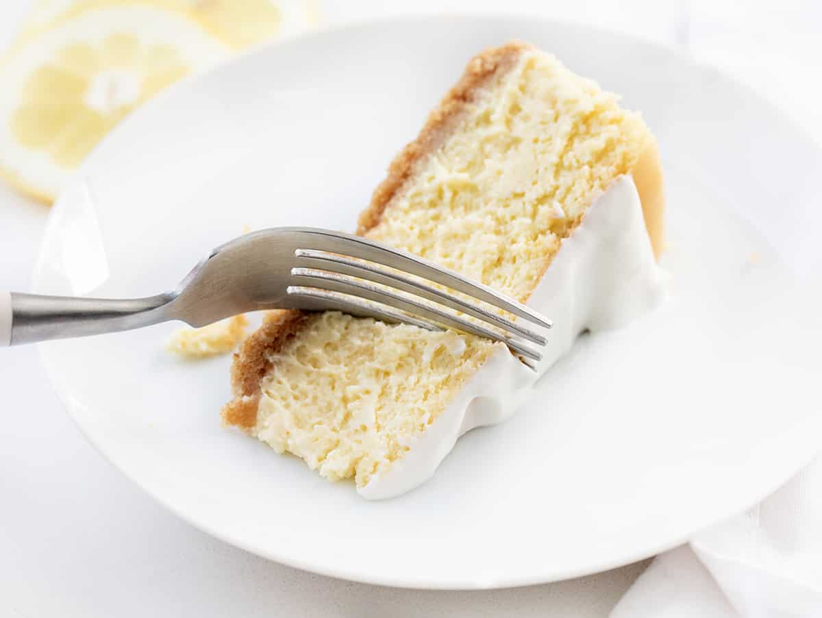 Piece of Lemon Cheesecake on a White Plate with a Fork Taking a Bite.