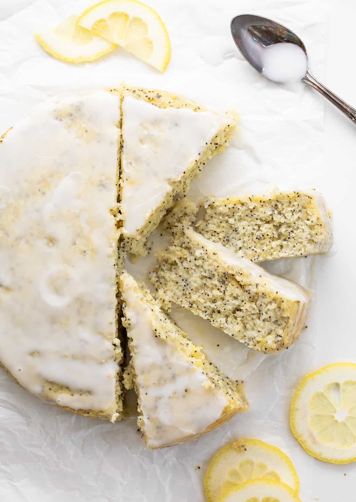 Whole Lemon Poppy Seed Cake on a White Piece of parchment Paper with Four Pieces Cut and Two Pieces on Their Sides Showing Tender Crumb.