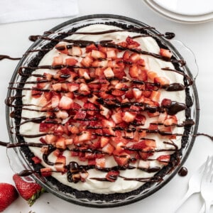 Overhead of a Chocolate Strawberry Marshmallow Pie on a White Counter with Hot Fudge Drizzle and Strawberries.