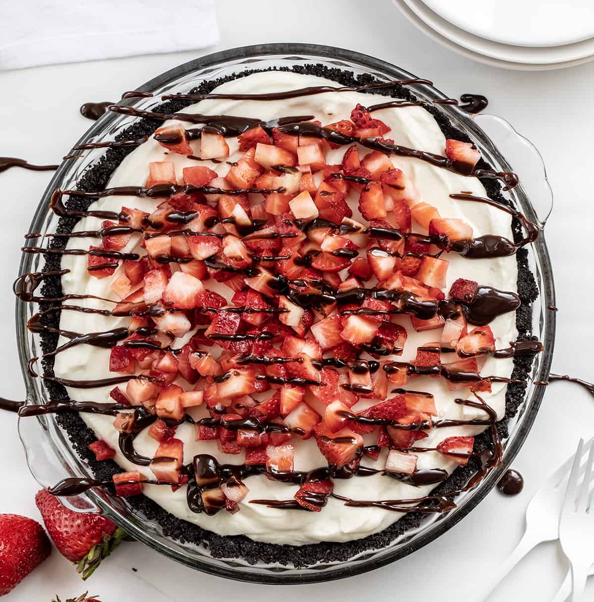 Overhead of a Chocolate Strawberry Marshmallow Pie on a White Counter with Hot Fudge Drizzle and Strawberries. 