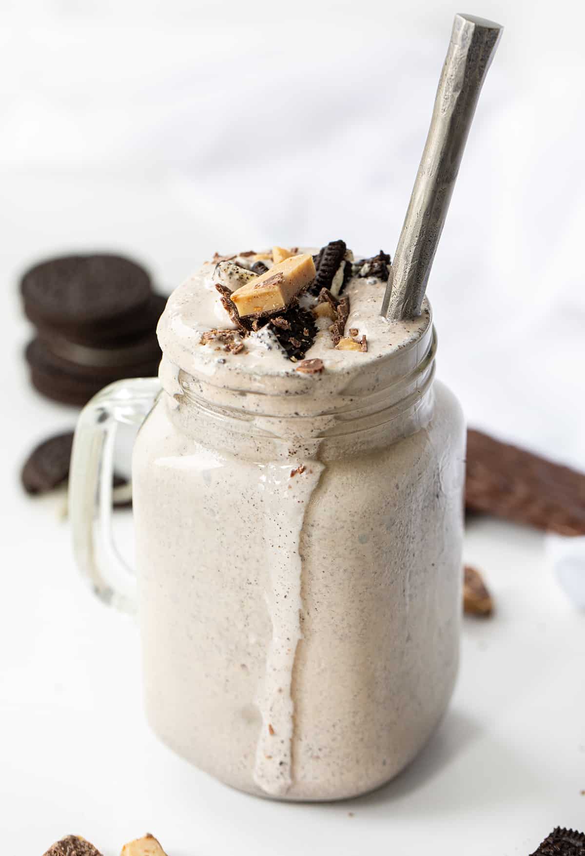 Mug of Oreo Heath Blizzard, a Recipe Adaptation Based on Dairy Queens Blizzard, and Surrounded by Oreos and Heath.