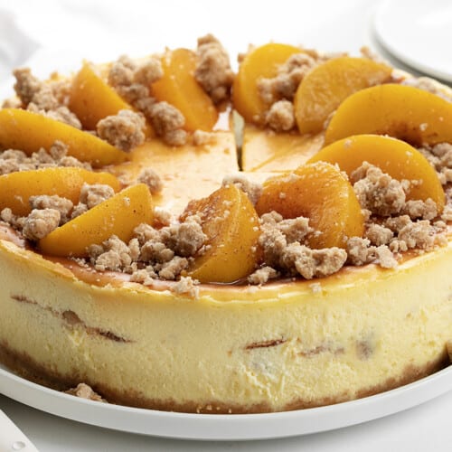 Peach Crumble Cheesecake on a White Platter on a White Counter with Forks.