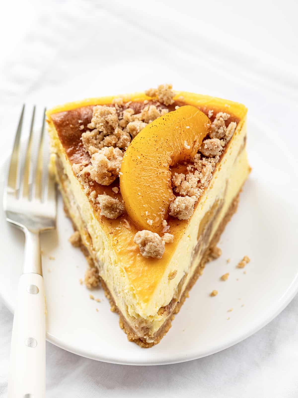 Slice of Peach Crumble Cheesecake on a White Plate with a White Fork.