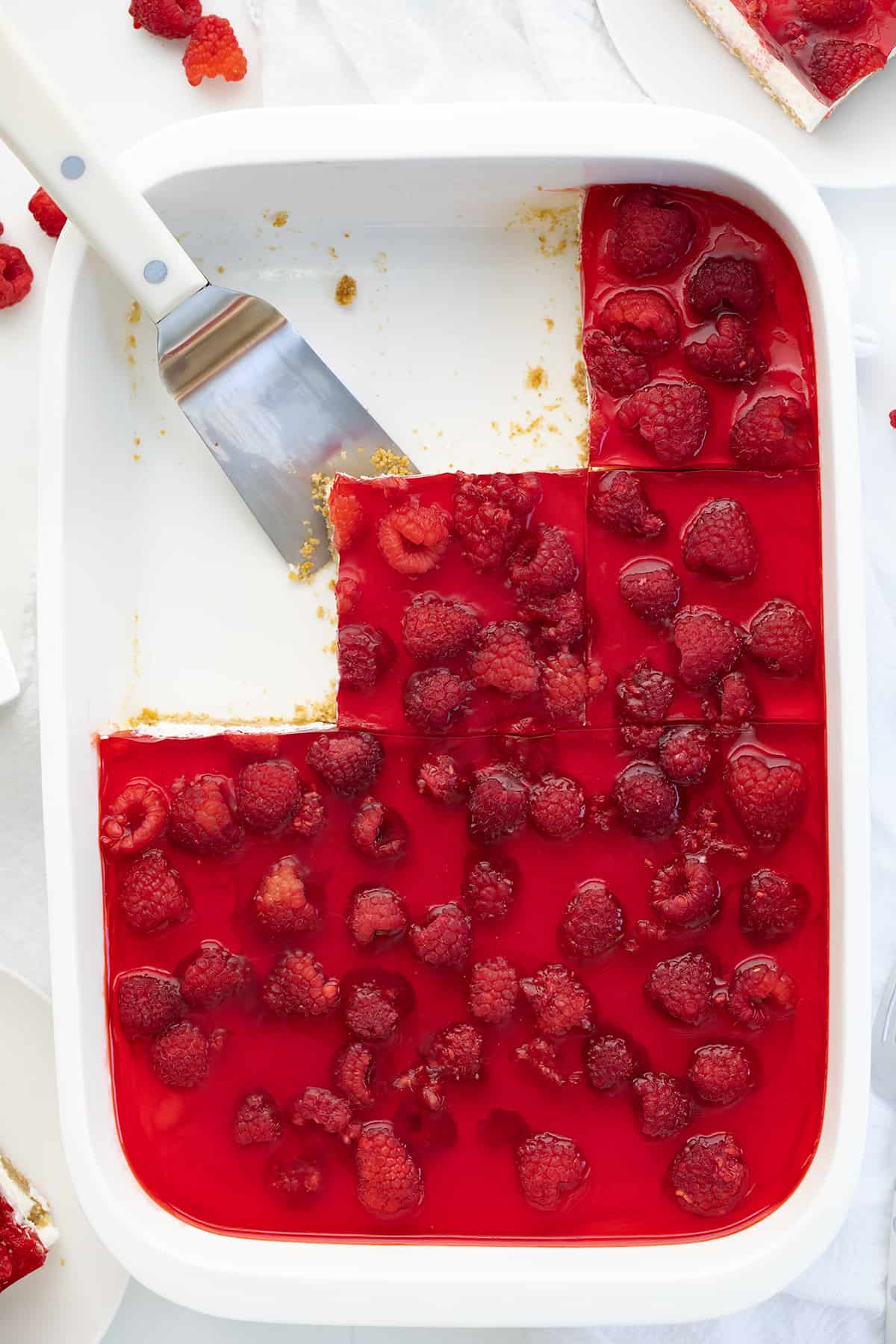 Looking Down on a Pan Filled with Raspberry Pretzel Salad with a Few Pieces Removed and a Spatula.