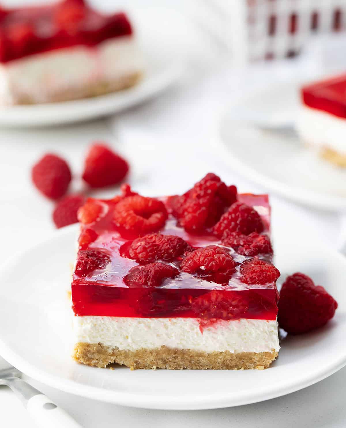 Raspberry Pretzel Salad on a White Plate with Fresh Raspberries Around and More in the Background.