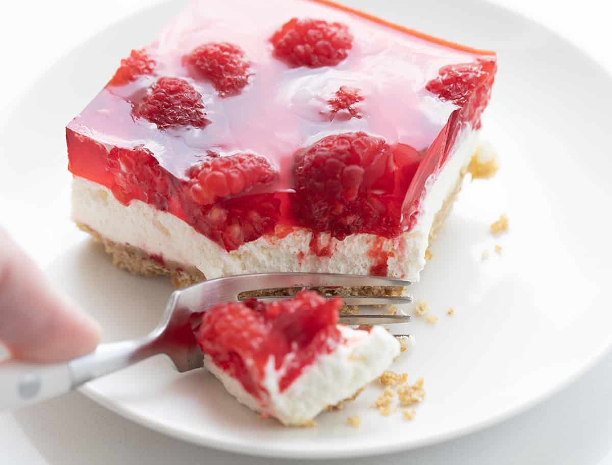 Fork Taking a Bite of Raspberry Pretzel Salad on a White Plate.