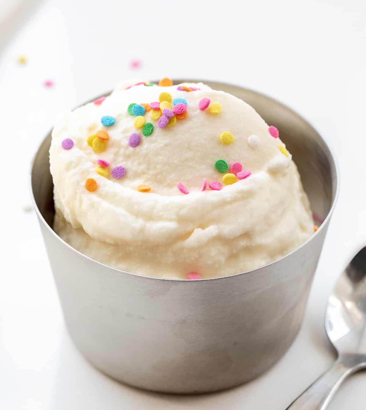 Metal Bowl with Scoops of Soft Serve Ice Cream in It with Sprinkles and a Spoon on a White Counter.