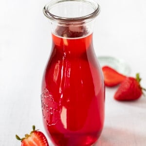 Bottle of Strawberry Simple Syrup Surrounded by Strawberries.