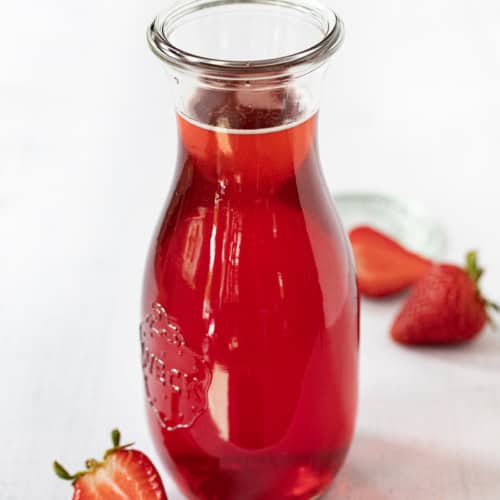 Bottle of Strawberry Simple Syrup Surrounded by Strawberries.