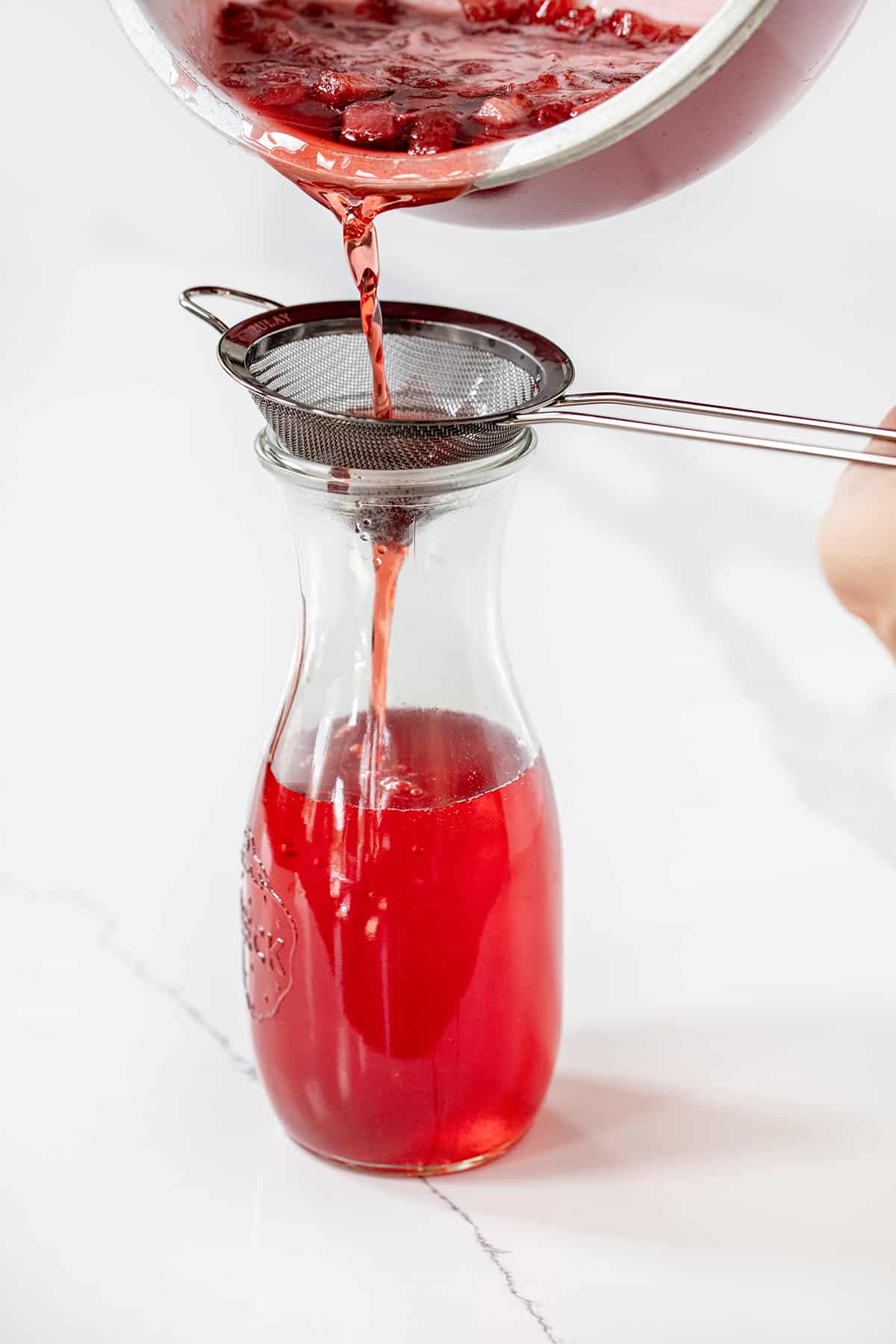 Straining Strawberry Mixture into Bottle to Make Strawberry Simple Syrup.