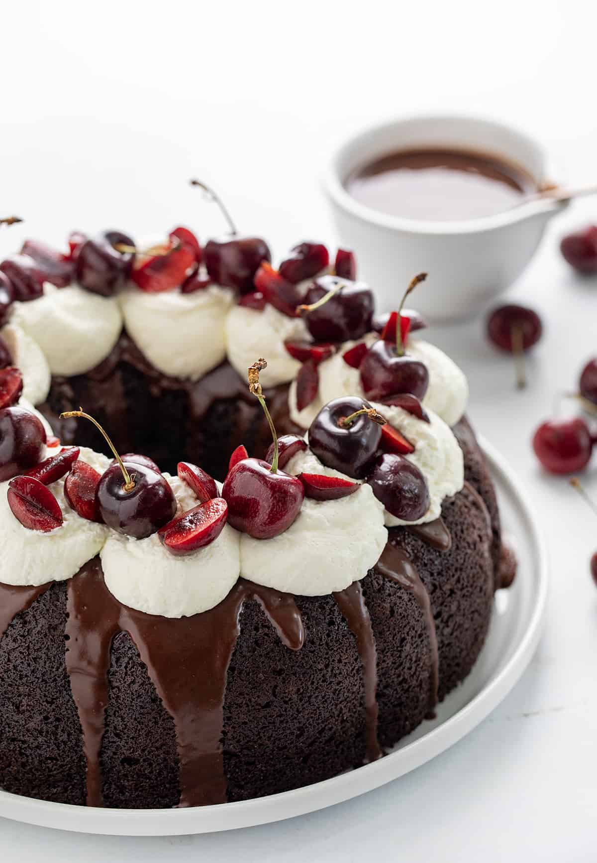 Close up of a Black Forest Bundt Cake on a White Counter Focusing on the Fresh Cut Cherries Sitting on Whipped Topping.