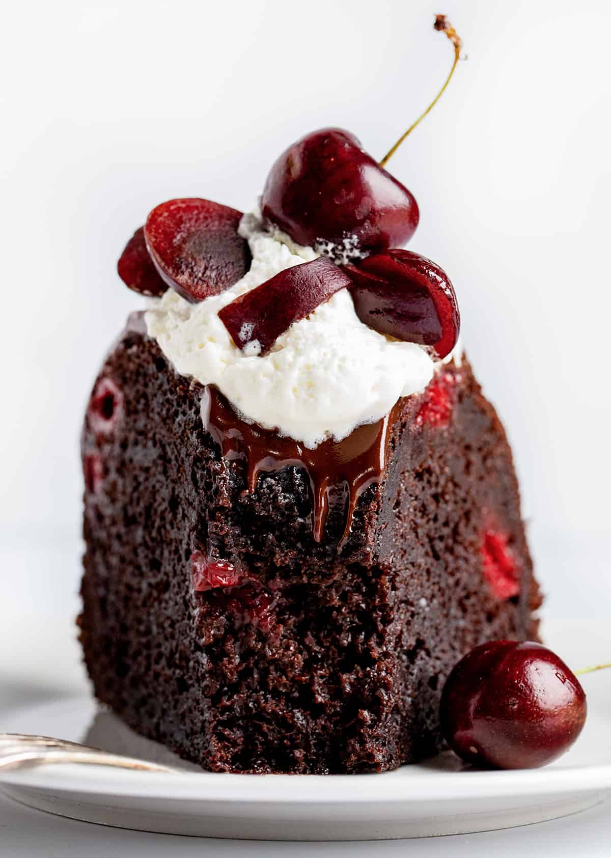 Piece of Black Forest Bundt Cake on a Plate Upright with a Bite Removed on a White Counter.