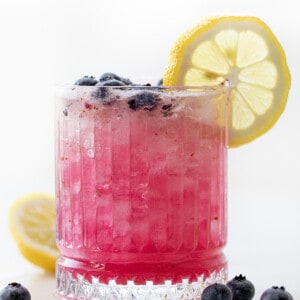 Glass of Spiked Blueberry Lemonade that is Backlit and Has a Lemon Wheel.