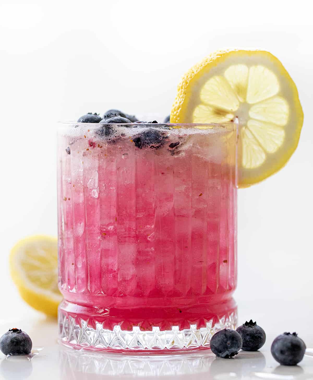 Glass of Spiked Blueberry Lemonade that is Backlit and Has a Lemon Wheel. 
