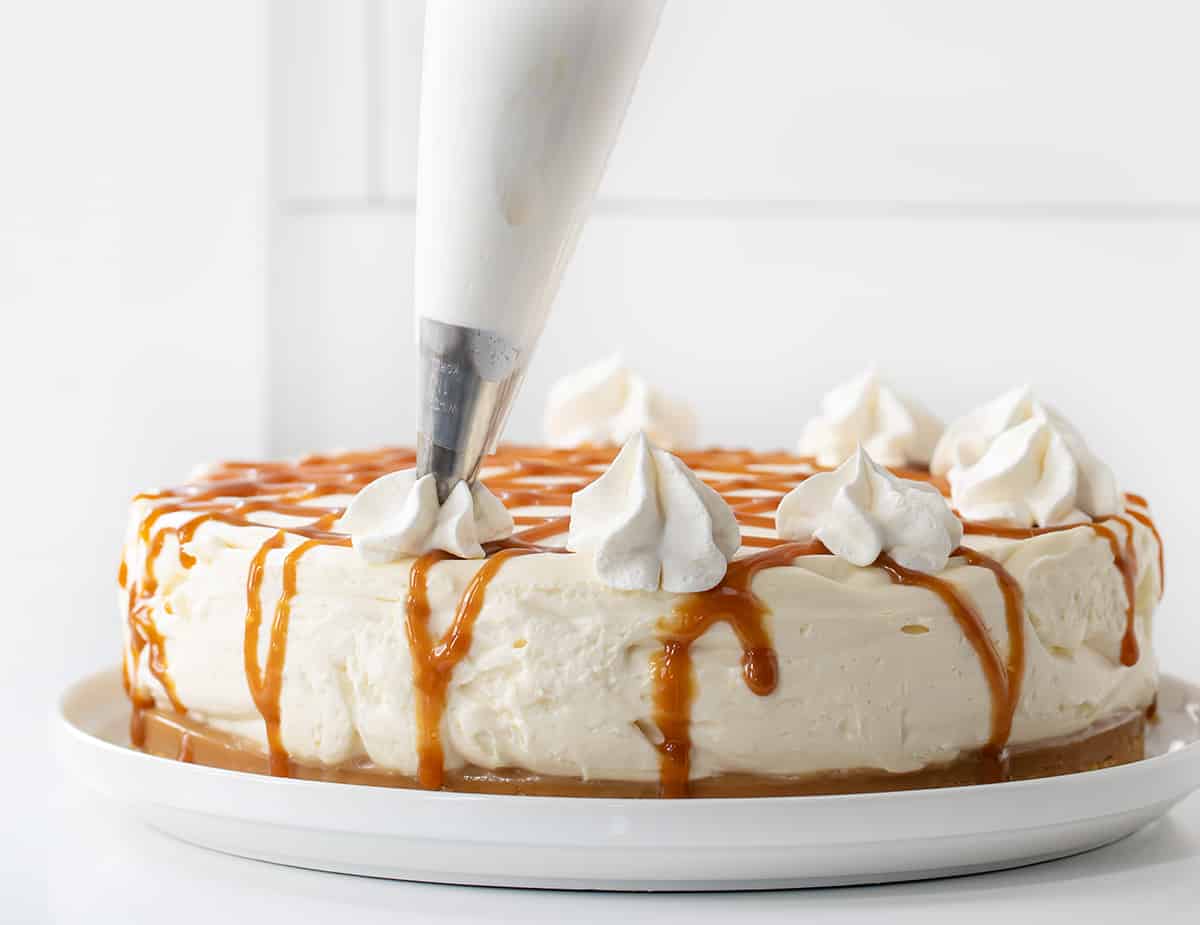 Adding Dollops of Whipped Topping to a Caramel Cheesecake on a White Plate.