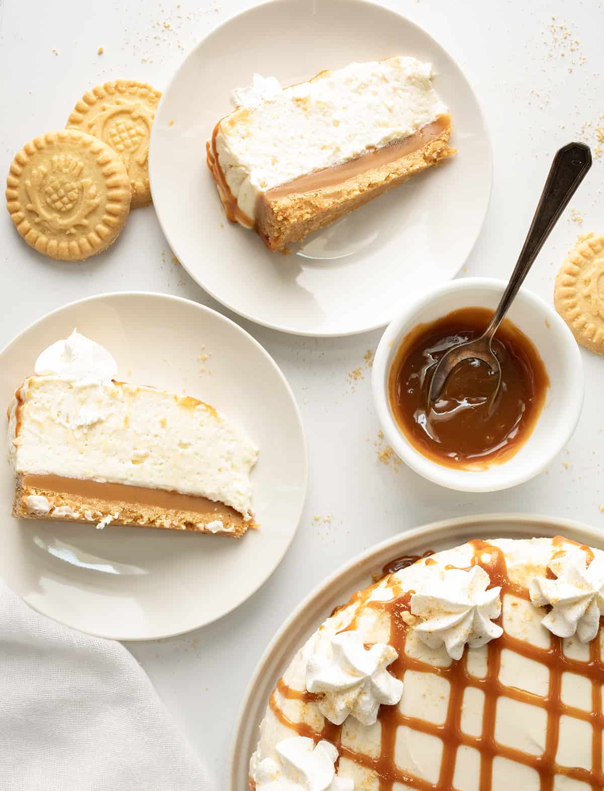 Pieces of Caramel Cheesecake on White Plates with a Bowl a Caramel Next to a Caramel Cheesecake.