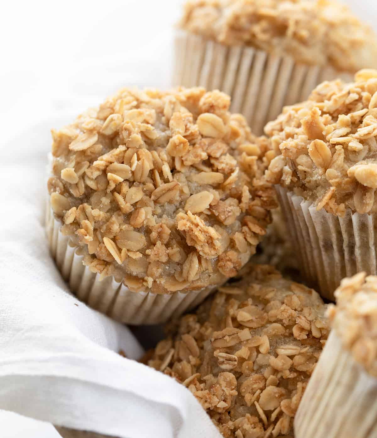 Close up of Banana Crunch Muffins in a Basket on a White Towel Showing Tops.