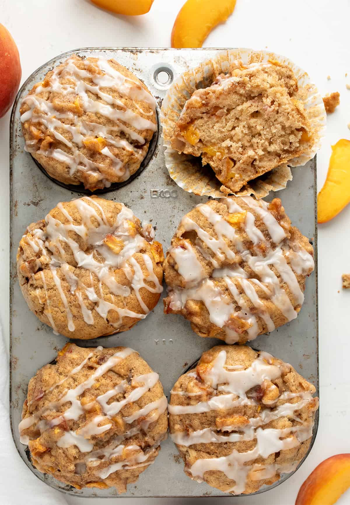 Peach Muffins in a Pan with One Cut in Half Showing Crumb on a White Counter.