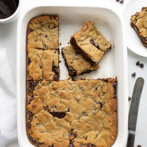 Pan of Hot Fudge Chocolate Chip Cookie Bars with Some Bars Removed and are Around the Pan on a White Counter from Overhead.