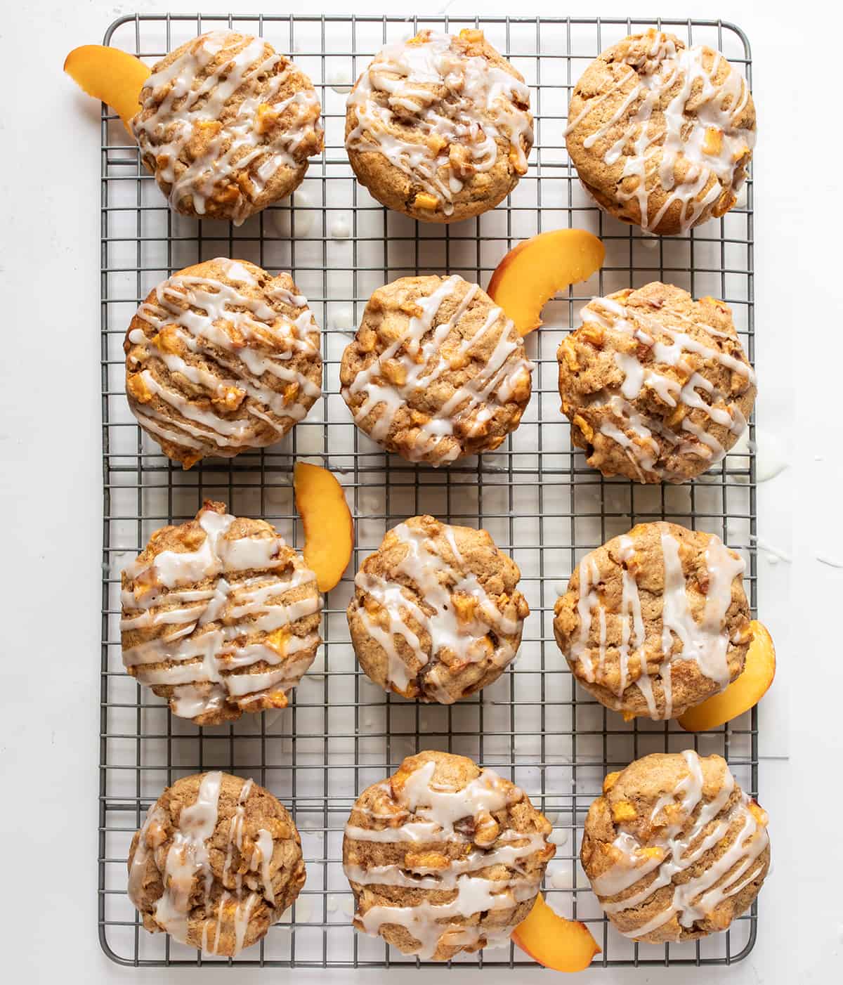 Peach Muffins on a Cooling Rack Covered in Glaze with a Few Peach Slices.