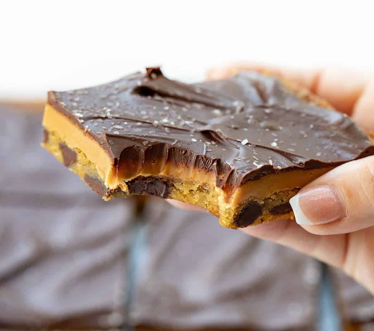 Hand Holding Salted Caramel Cookie Bar with a Bite Taken out of It.