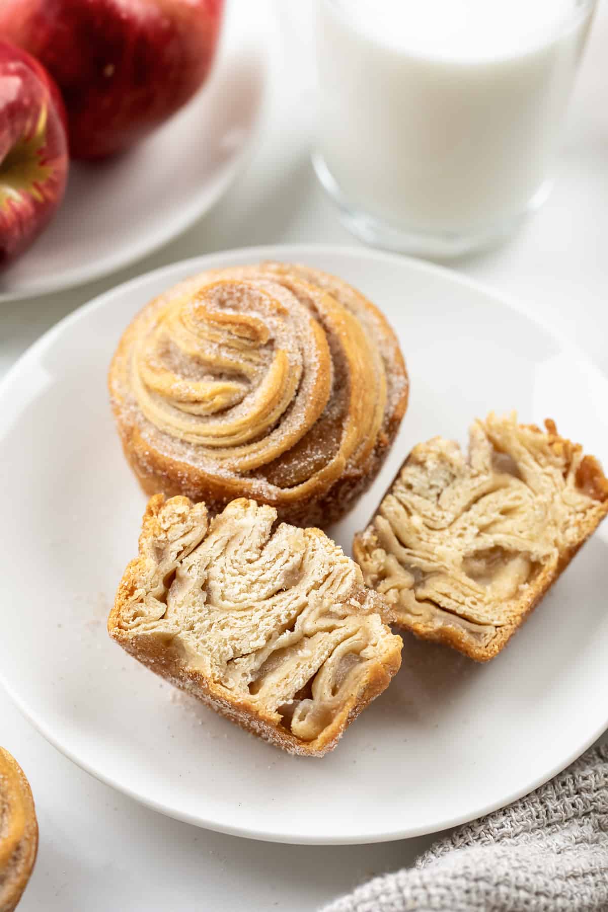 Apple Pie Cruffins on a white plate with one cut in half showing the apple pie filling inside.