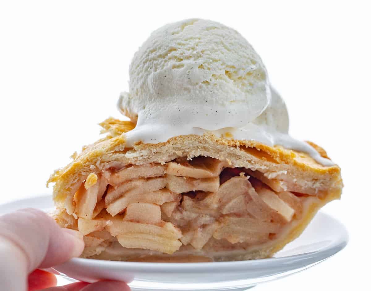 Hand Holding White Plate with a Piece of Bourbon Apple Pie on it with Ice Cream.