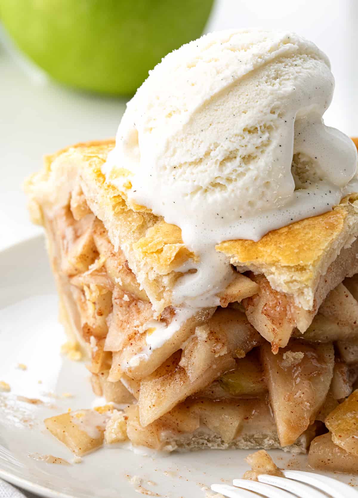 Close up of Bourbon Apple Pie Piece on a Plate with Melting Ice Cream on Top.