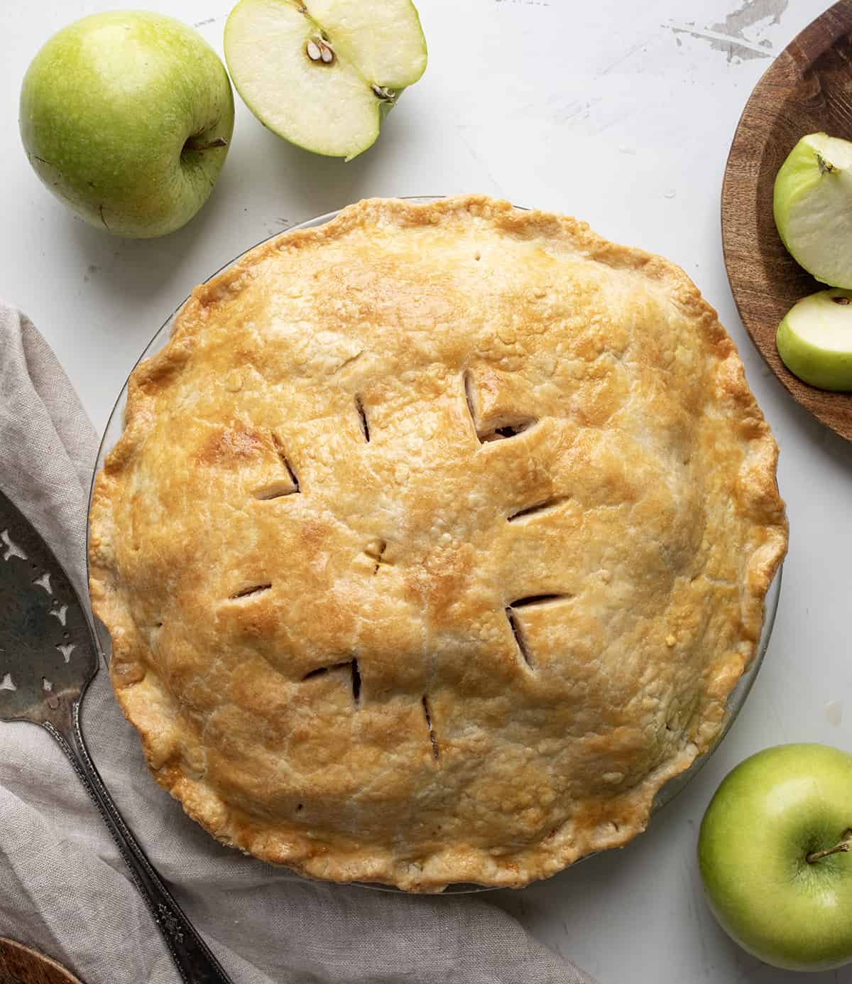 Whole Bourbon Apple Pie on a White Table with Apples and Towel. 