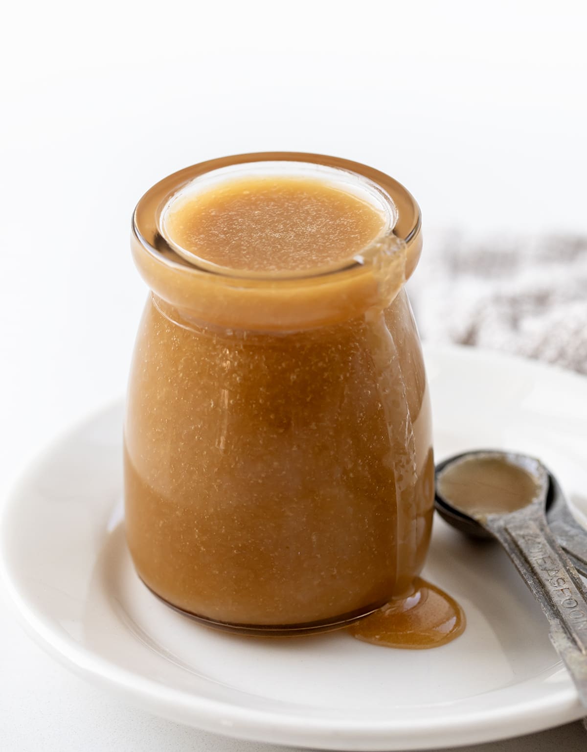 Glass Jar Overflowing Butterscotch Sauce on a White Plate with Measuring Spoons.