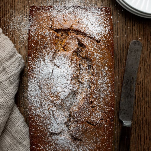 Whole Gingerbread Loaf on a Table with a Knife and Towel Next to it From Overhead.