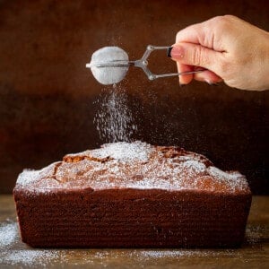 Sprinkling Confectioners Sugar over Gingerbread Loaf on a Dark Table.