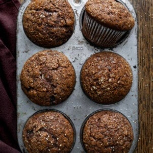 Gingerbread Muffins in a 6-spot muffin pan with one muffin on its side on a dark table.
