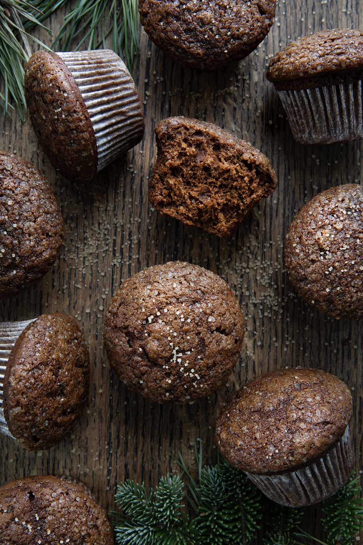 Gingerbread Muffins on a Dark Table with Muffins scattered aaround and one halved showing inside texture. 