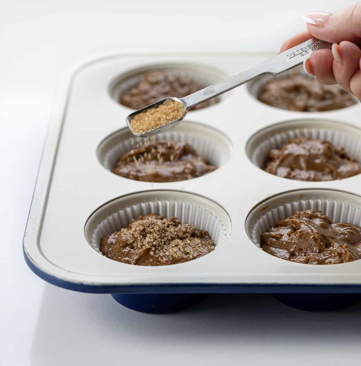 Raw Gingerbread Muffins batter in a muffin pan and adding turbinado sugar on top.