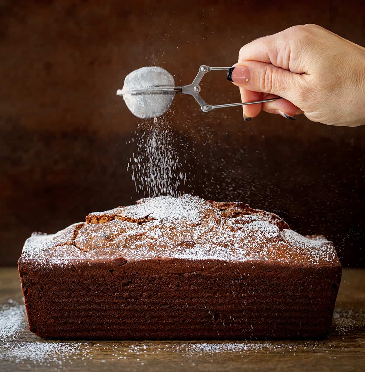 Sprinkling Confectioners Sugar over Gingerbread Loaf on a Dark Table.