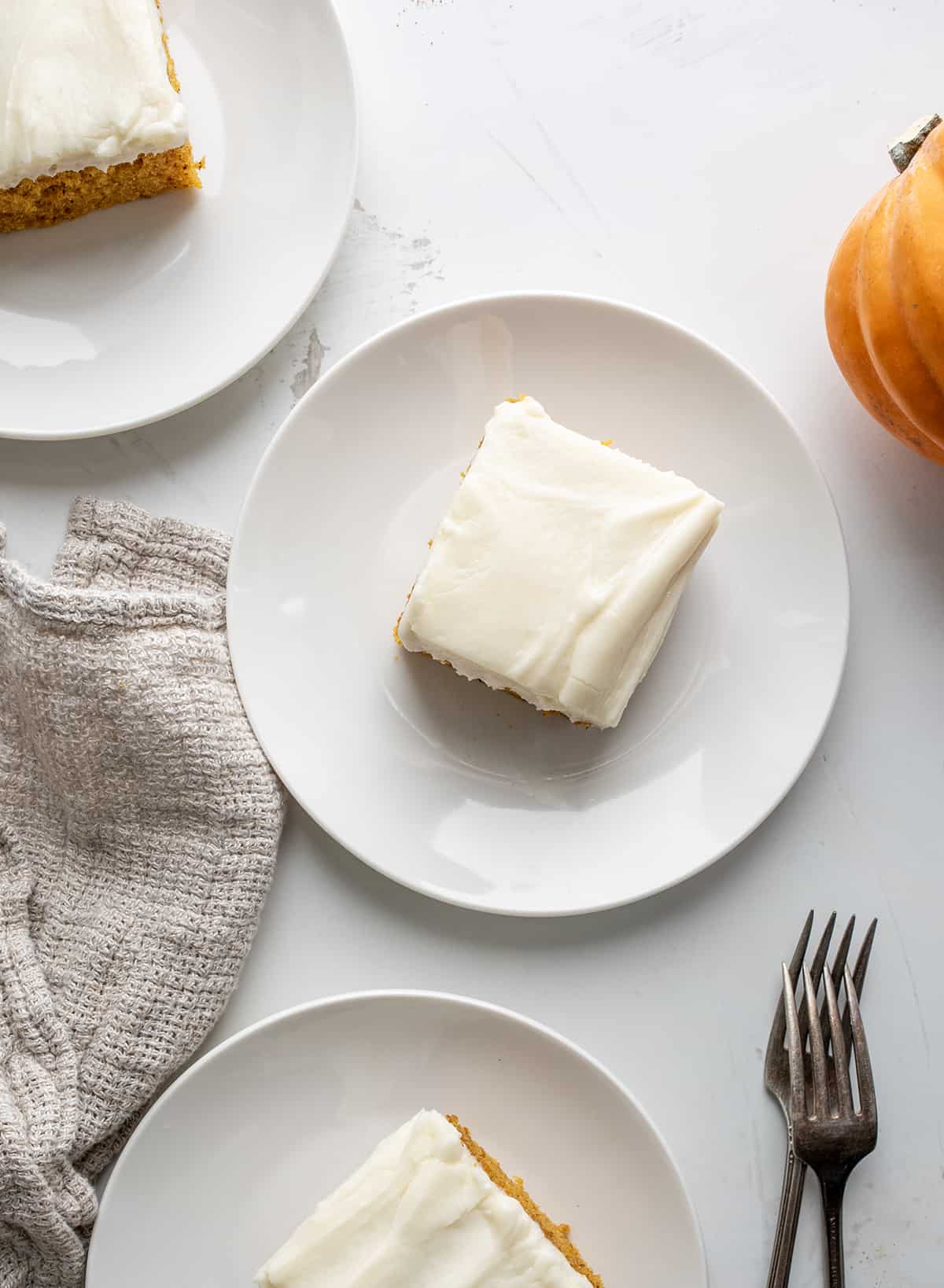 Plates of Pumpkin Bars with Cream Cheese Frosting on a White Table.