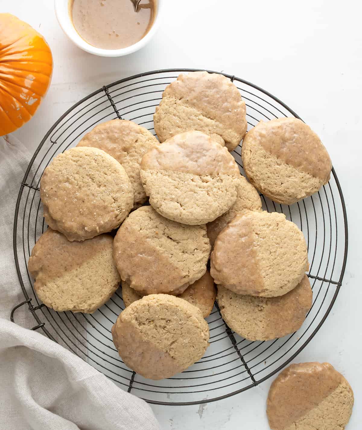 Tray of Pumpkin Spice Butter Cookies on a White Table with Towel and Glaze in a bowl from Overhead. 