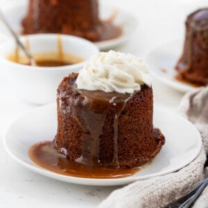 One Sticky Toffee Pudding on a plate with more sauce and others behind.