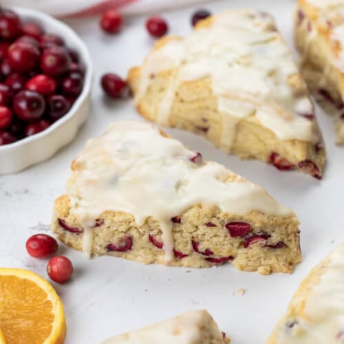 Cranberry Orange Scones next to fresh cranberries and orange slices on a white counter.