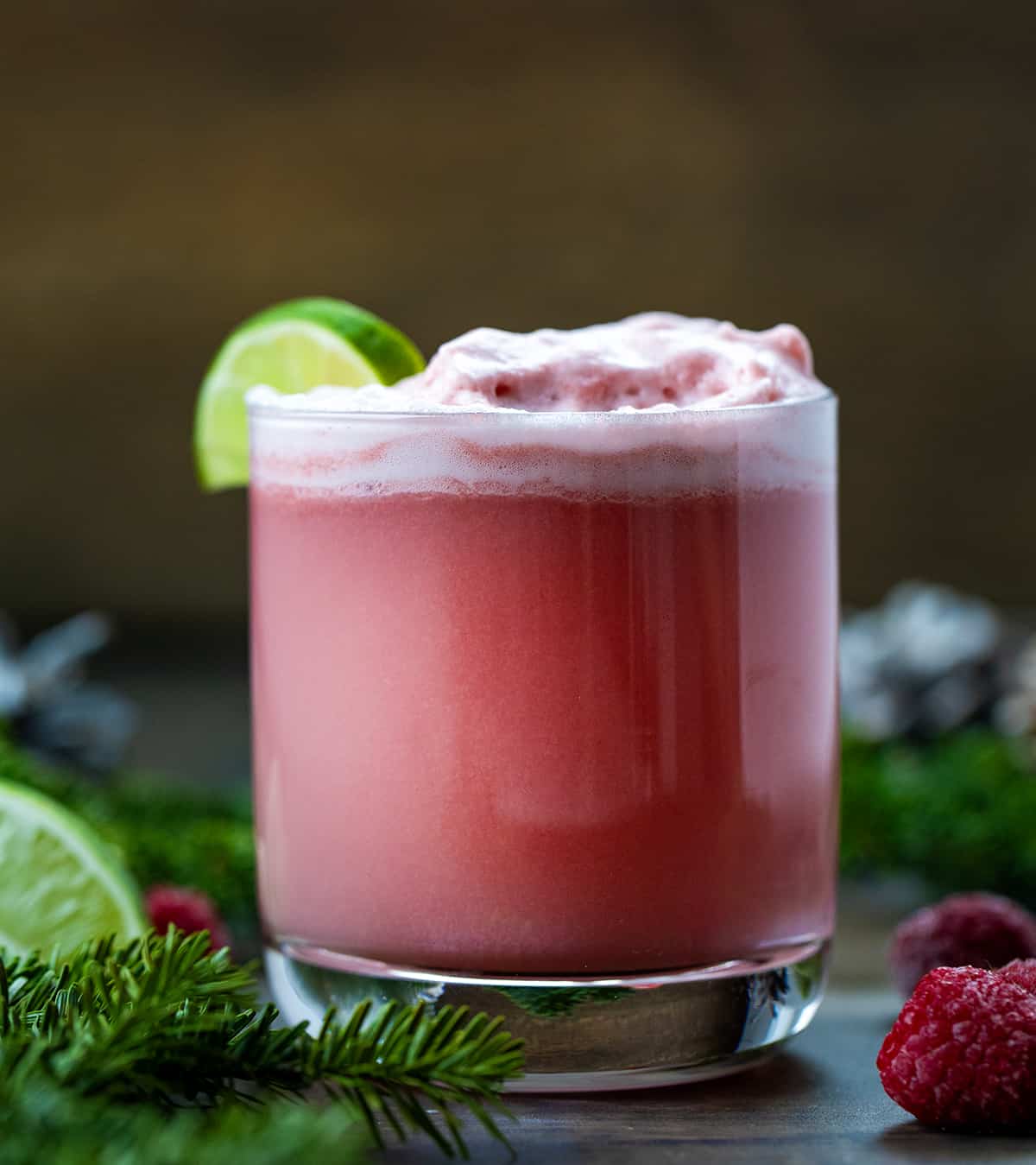 One glass of Sherbet Christmas Punch on a table with raspberries and pine.