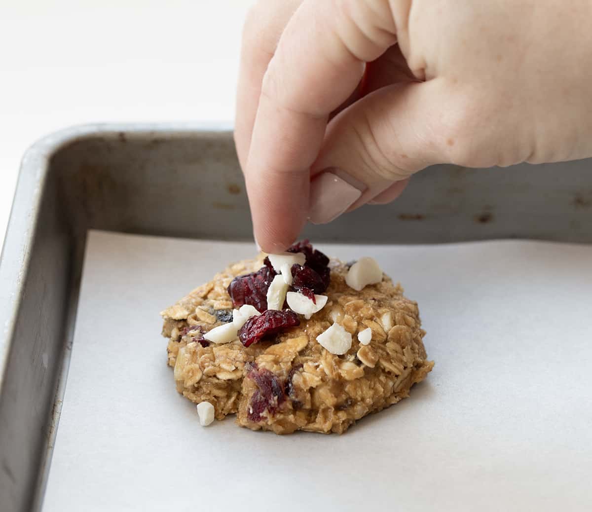 Adding toppings to White Chocolate Cranberry Oatmeal Cookies before baking.