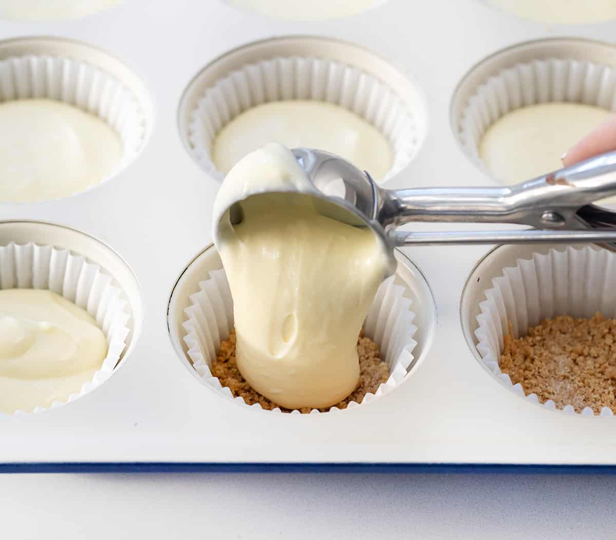 Scooping cheesecake batter into cups before baking.