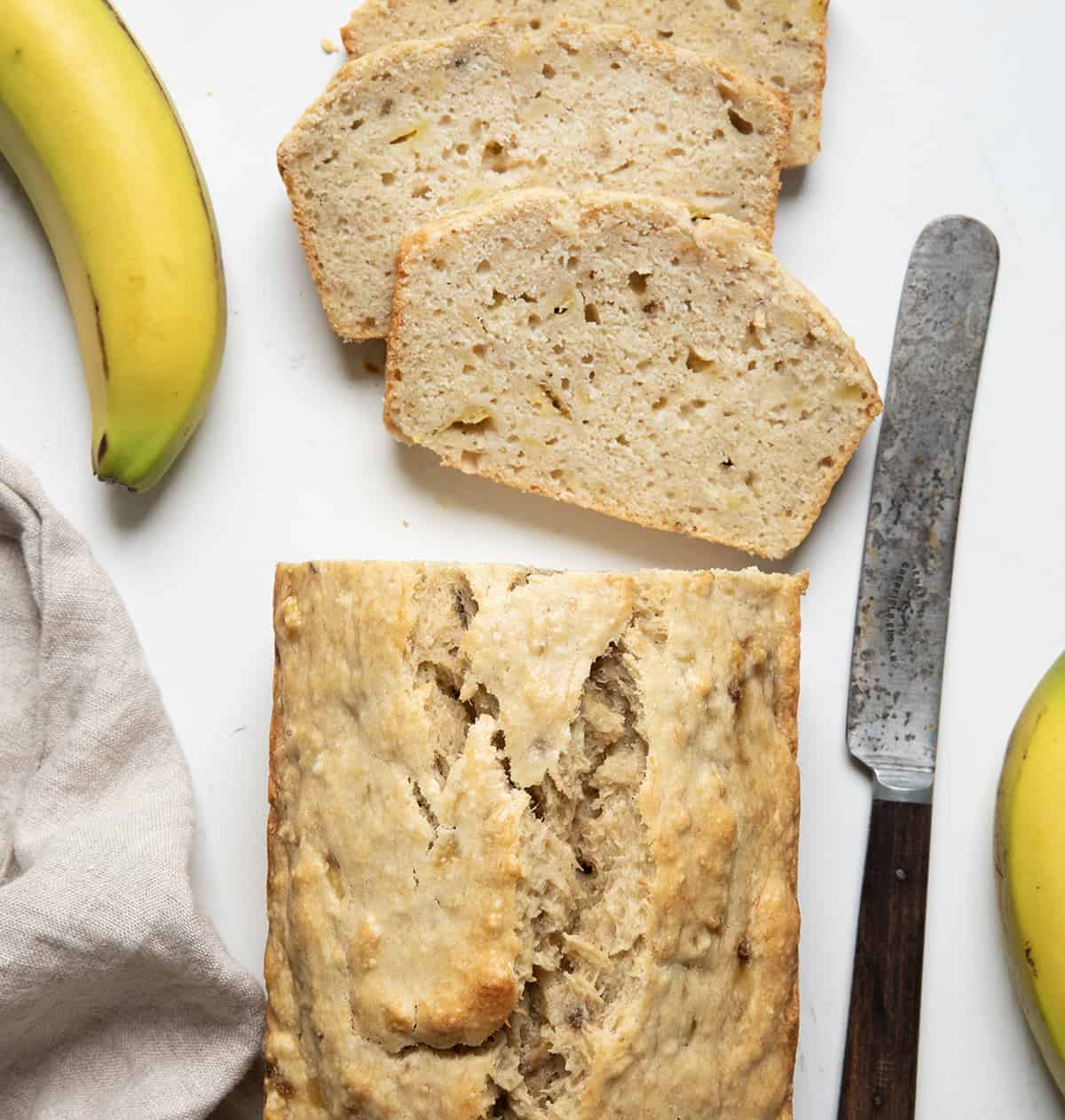 Bisquick™ Banana Bread on a counter with pieces cut and bananas.