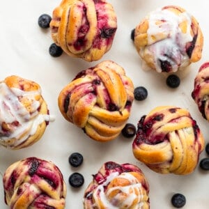 Muffin Tin Braided Blueberry Rolls on a white counter with fresh blueberries from overhead.